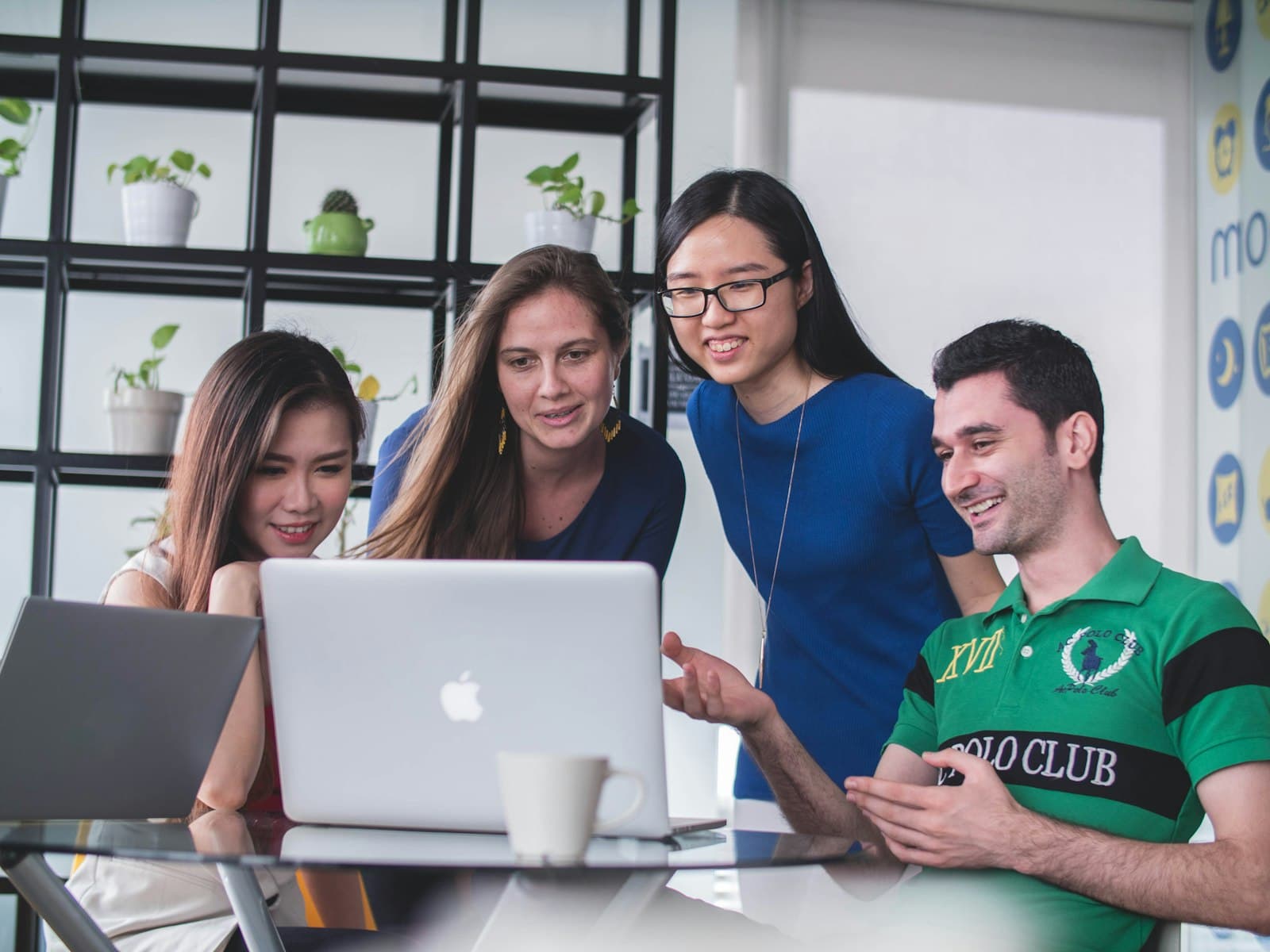 Four colleagues gathered around a laptop, smiling as they review work together
